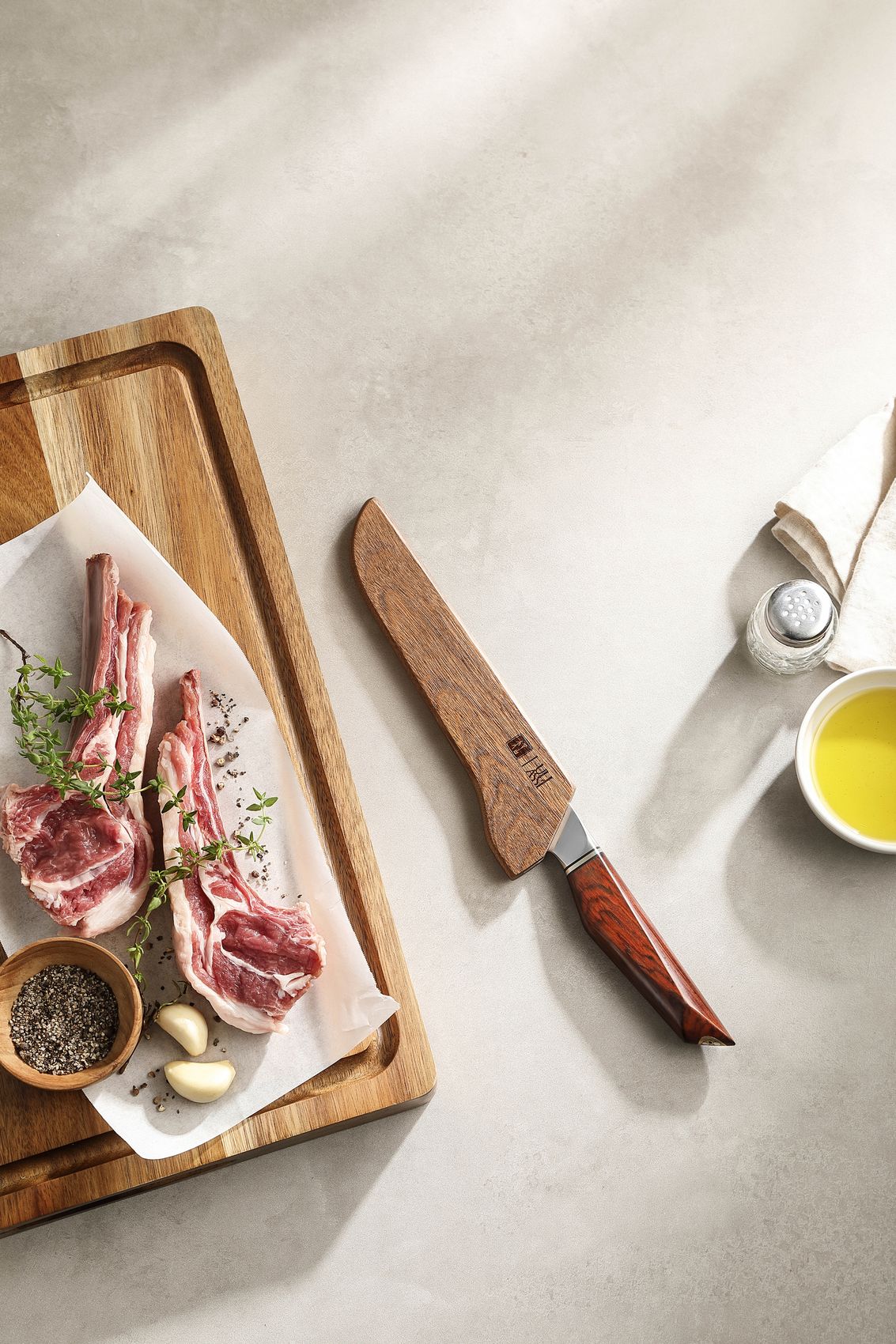 The boning knife in its wooden saya sheath resting beside a board of raw lamb rack, herbs, garlic and olive oil