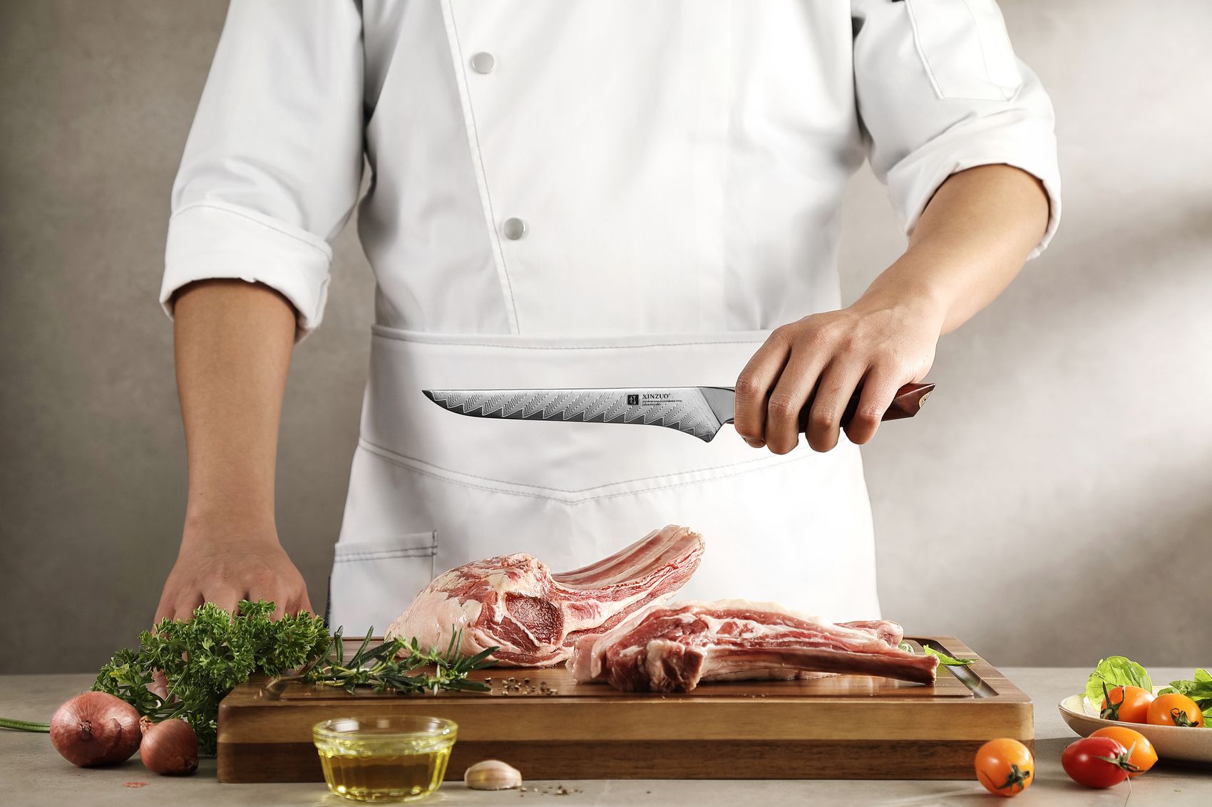 Chef in white gripping the boning knife over raw lamb racks on a wood board, showing the handle grip and blade
