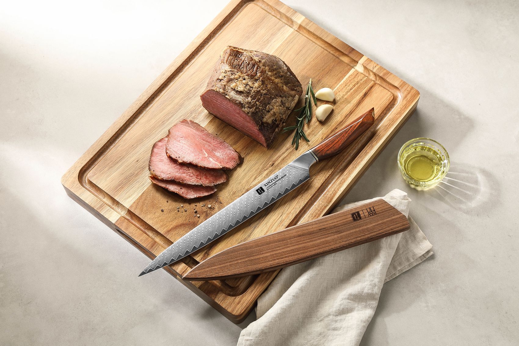 Carving knife resting on a board beside sliced roast beef, rosemary and olive oil