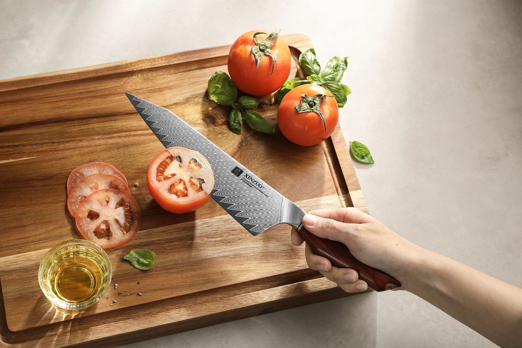 Hand slicing a ripe tomato with the Damascus bunka knife on a wooden cutting board