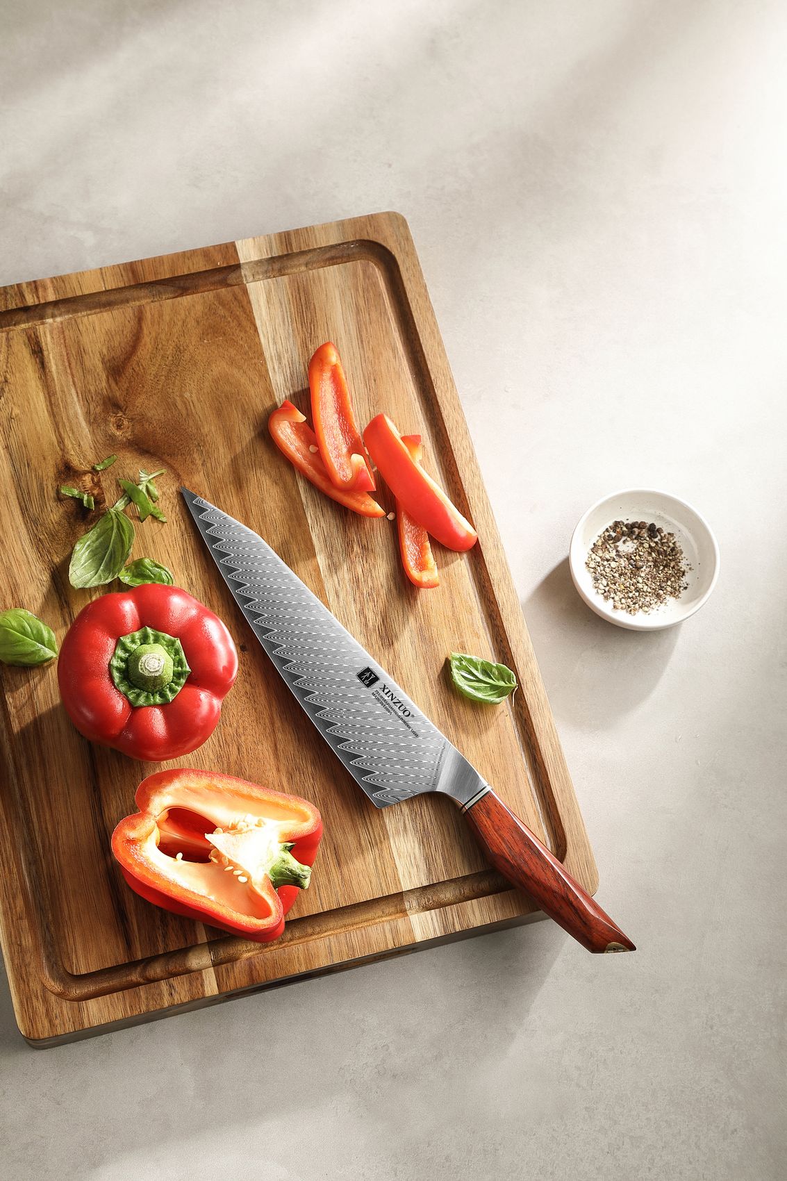 Damascus bunka chef knife on a wooden board with fresh capsicum and peppercorns