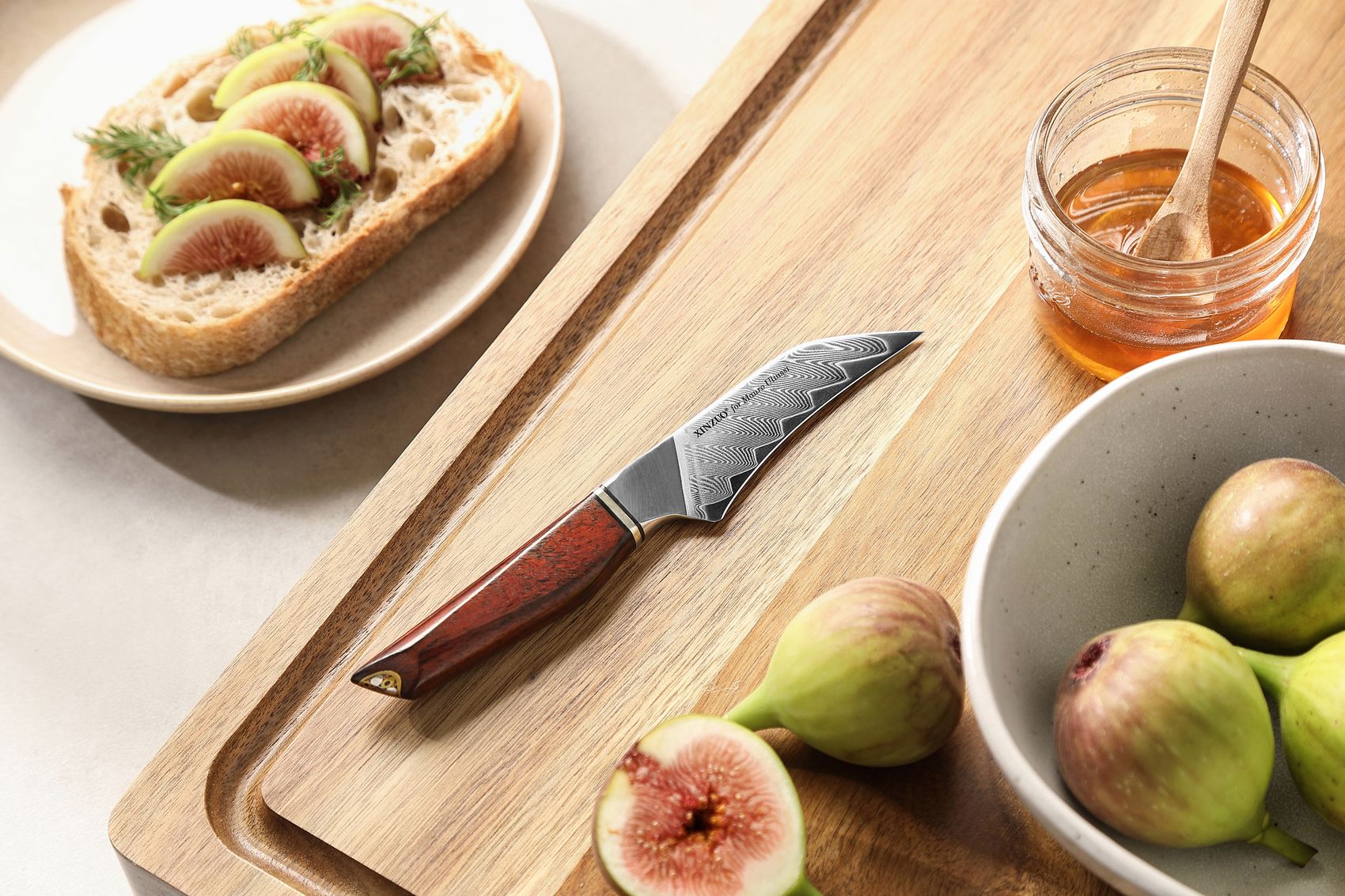 Damascus paring knife on a wooden board with fresh figs, a honey jar and fig-topped sourdough