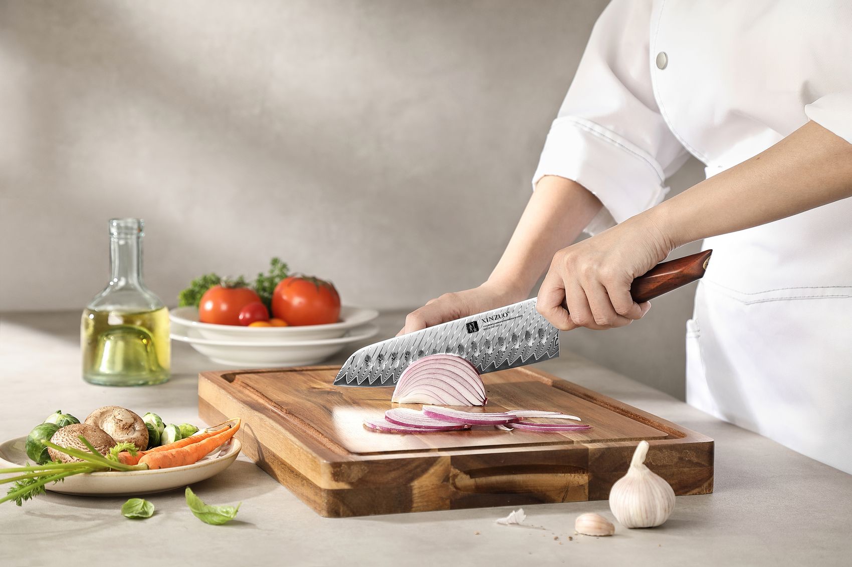 Chef in white uniform slicing red onion with the Santoku knife on a wooden board
